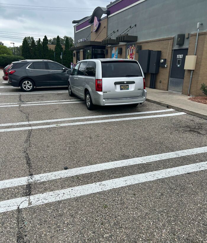 Silver van selfishly parked over multiple spaces in a busy parking lot, showing lack of common decency and respect for others.