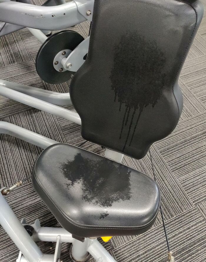 Sweat stains on a black gym machine seat and backrest showing selfish people lost common decency at the gym.