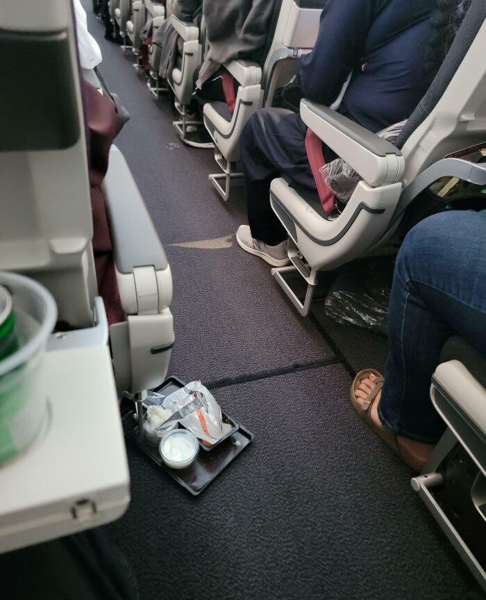 Discarded trash left on airplane floor between seats, showing selfish behavior and lack of common decency on a flight.