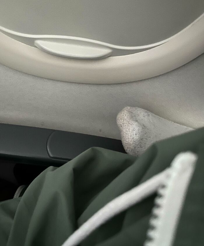 Passenger with socks resting on airplane window frame showing selfish behavior making life harder for everyone else.