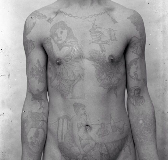 Black and white photo of a man with multiple tattoos from weird history pics showing unusual body art from the past.