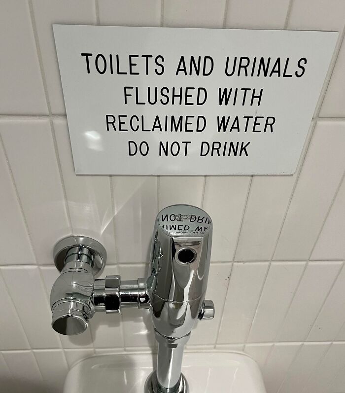 Sign above a restroom flush valve warning toilets and urinals are flushed with reclaimed water, a hilariously random message.