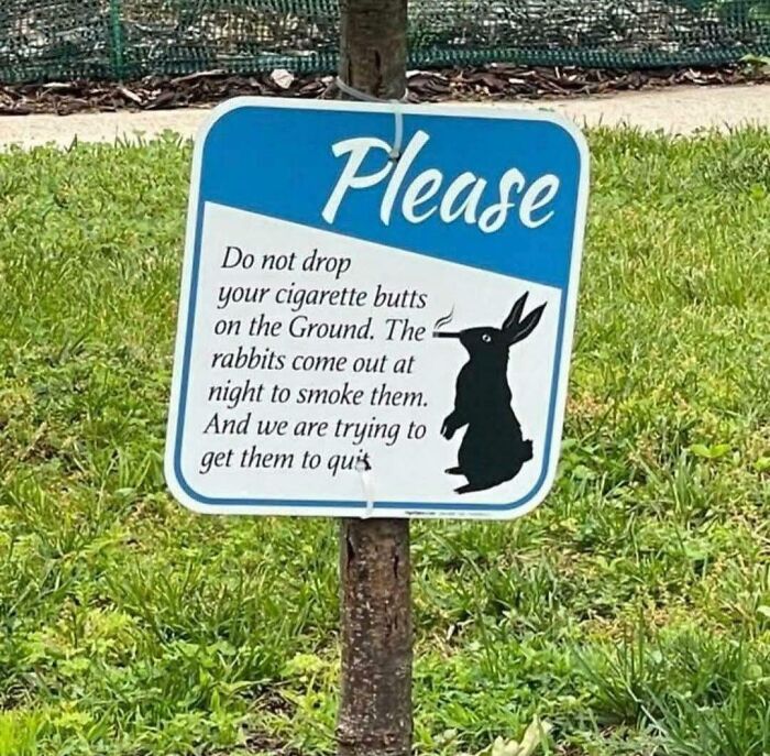 Humorous sign warns against dropping cigarette butts to help rabbits quit smoking in a green outdoor setting.
