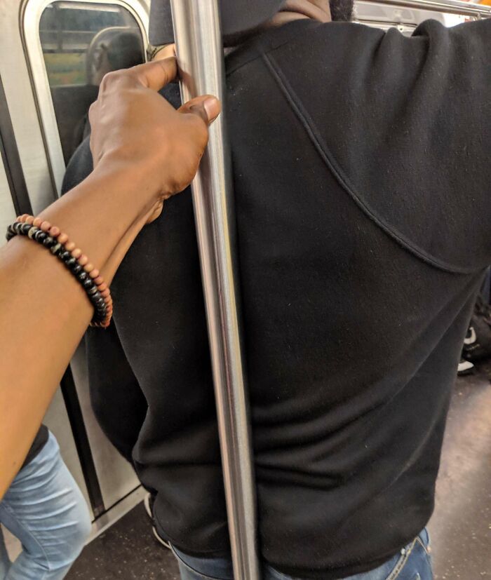 Hand holding metal pole on crowded subway, illustrating selfish people causing discomfort and making life harder for others.