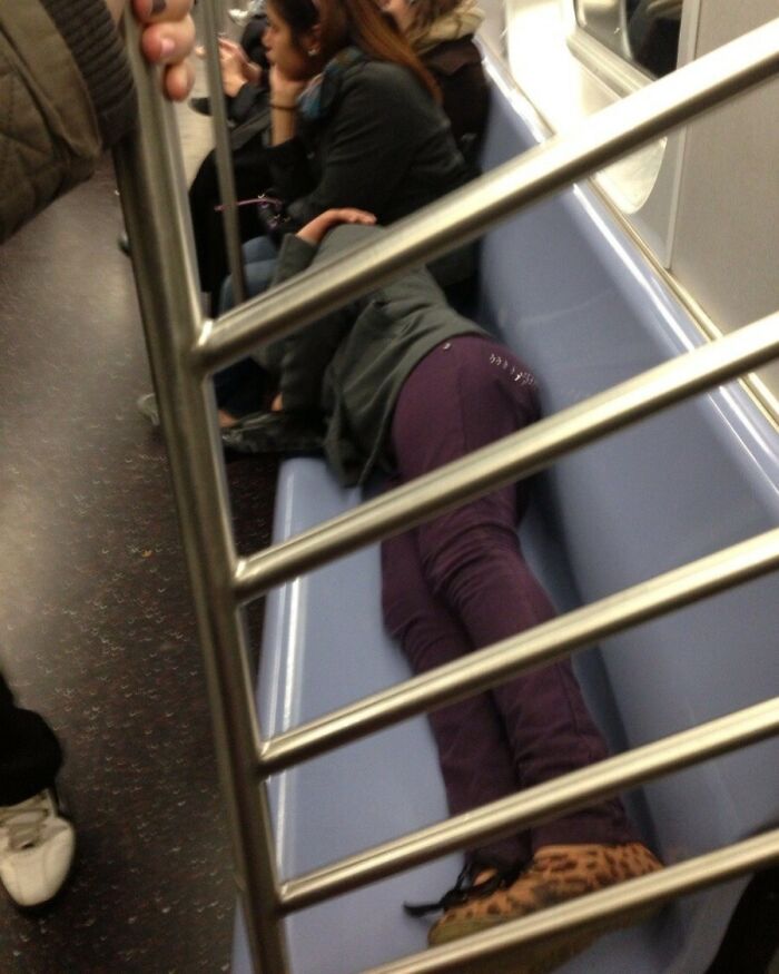 Person lying across multiple seats on a crowded subway, showing selfish behavior making life harder for others.