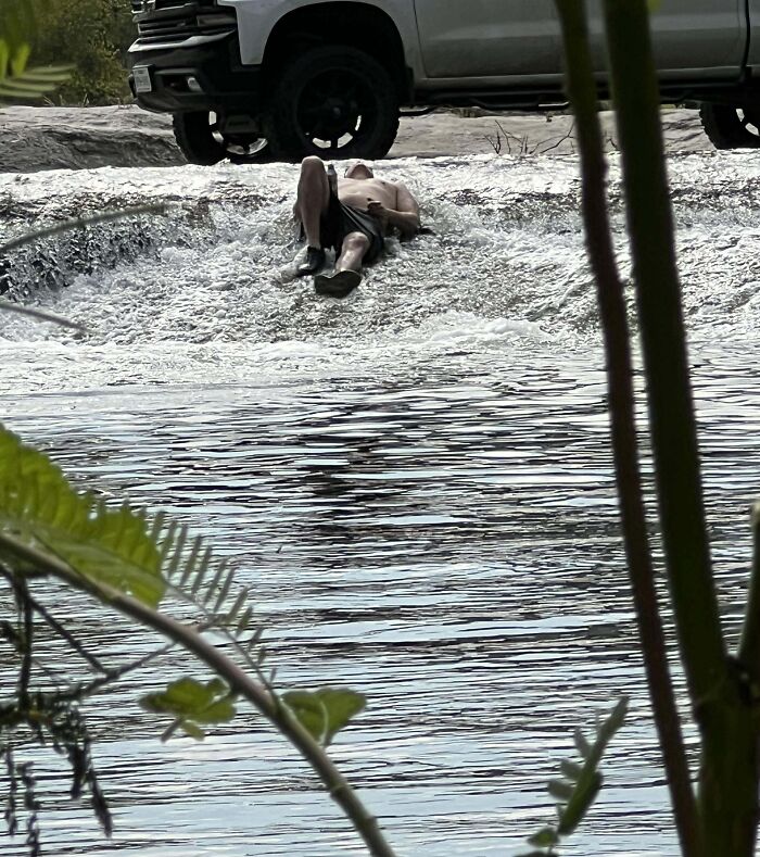 Man lying on rushing water as a truck is parked near the shore showing selfish people making life harder for others