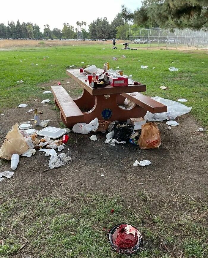 Picnic table covered in trash and litter scattered across grass showing selfish people lost common decency behavior outdoors