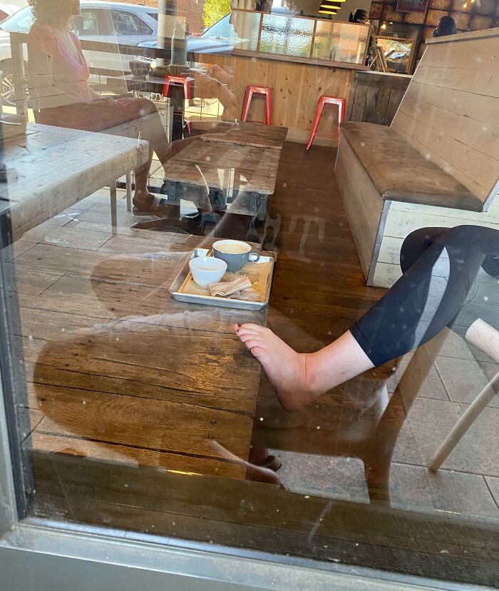 Cafe interior with a person resting bare feet on a table, highlighting selfish people losing common decency in public spaces.