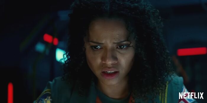 A woman with curly hair looking worried in a dark room, representing disappointing Netflix movies and letdowns.