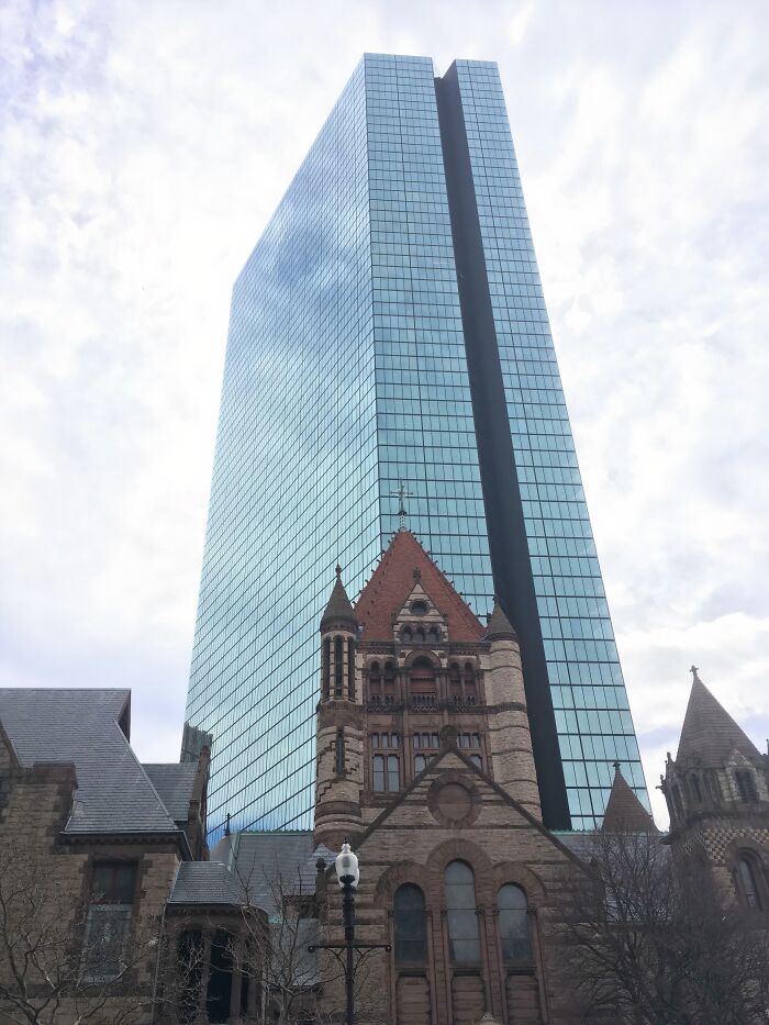 Old versus modern architecture with a historic stone building in front of a tall glass skyscraper against a cloudy sky