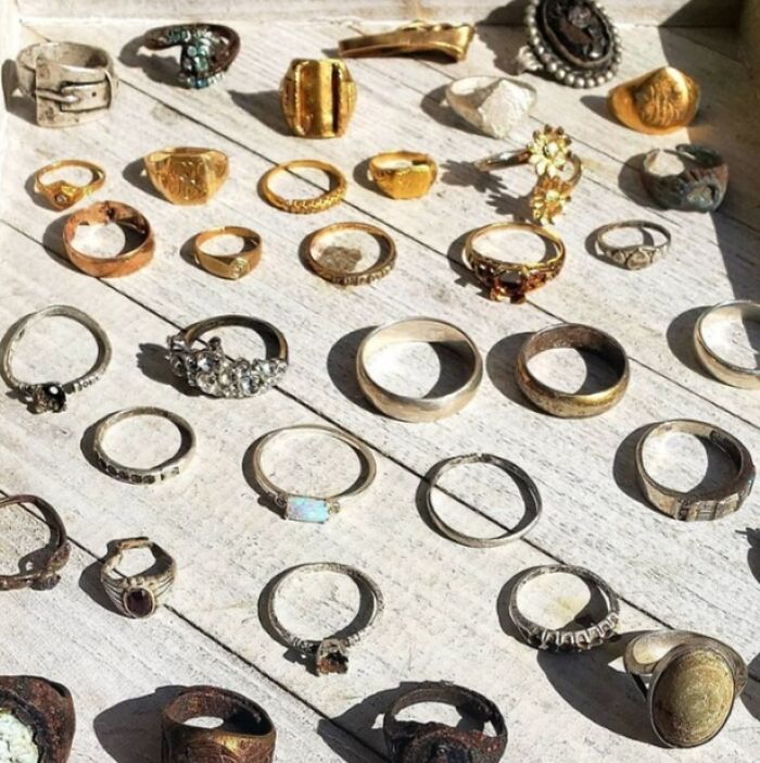 Collection of interesting and bizarre rings and jewelry found at the beach, showcasing unique and aged pieces on a wooden surface.