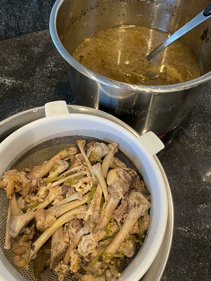 Cooked chicken bones and broth in metal pots showing restaurant kitchen prep for unusual orders.