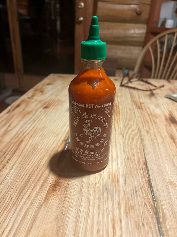 Bottle of Sriracha hot chili sauce on a wooden table representing restaurant workers handling unusual orders.