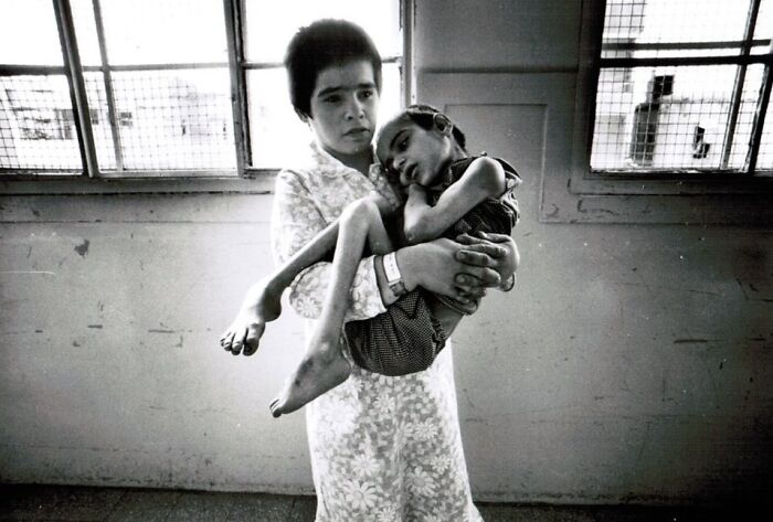 Young woman carrying a frail child in a hospital room, a poignant weird history pic showing past hardships.