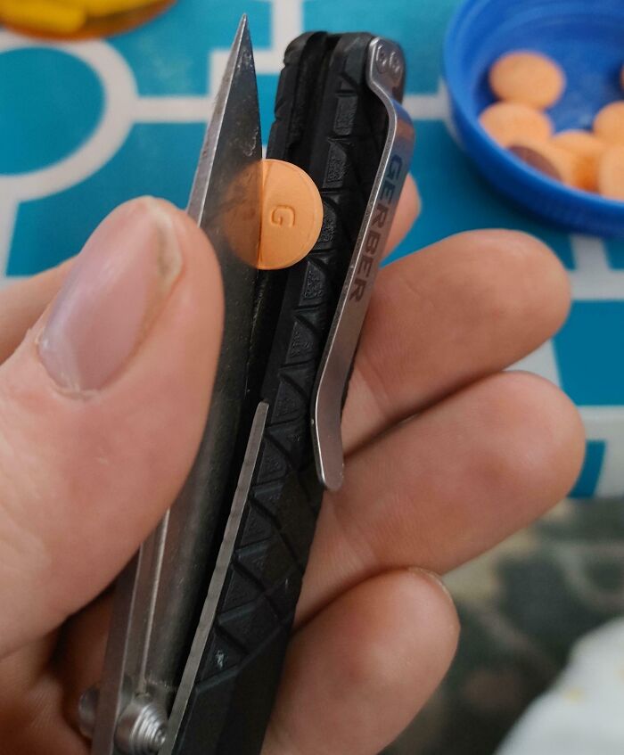 Close-up of a person using a multi-tool knife to carefully cut a small round tablet, demonstrating genius life hacks.