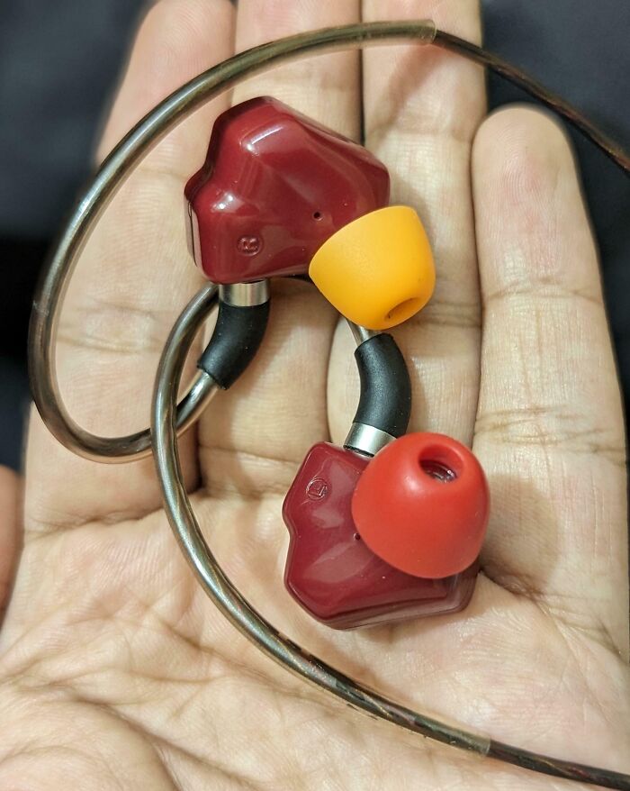 In-ear wired earphones with red and yellow tips held in palm, demonstrating genius life hacks for everyday use.