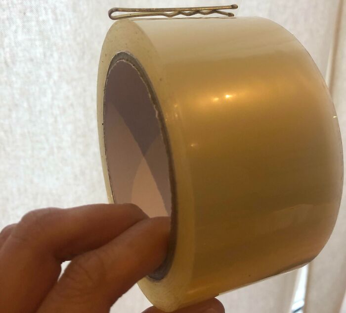 Hand placing a bobby pin on clear packing tape roll demonstrating a genius life hack people actually use.