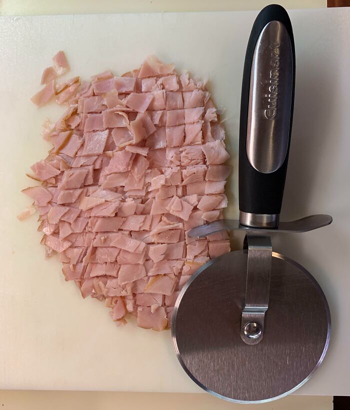 Pizza cutter slicing thin, evenly diced ham pieces on a white cutting board showing genius life hacks.