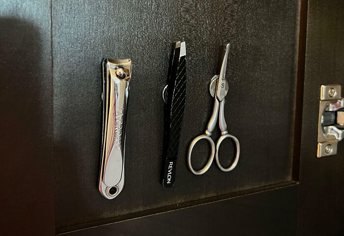 Nail clipper, tweezers, and scissors attached inside a cabinet door showcasing genius life hacks for organization.