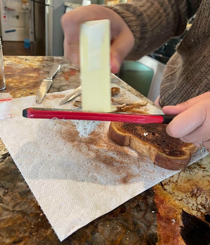 Person using a phone case as a grater to shred butter onto toast in a kitchen demonstrating genius life hacks in use