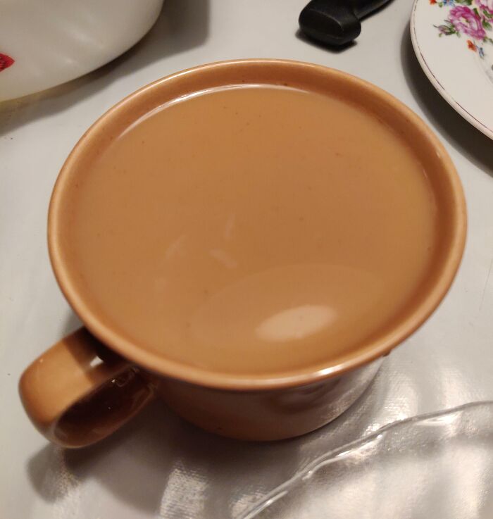 Coffee in a cup matching the color of its surroundings, blending in seamlessly with the cup and table setting.