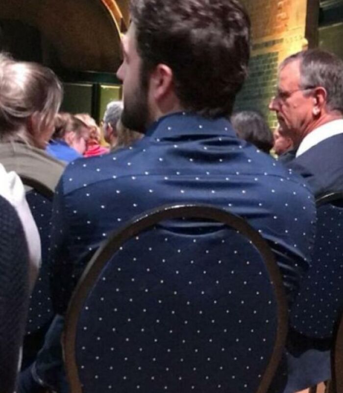 Man wearing a navy polka dot shirt sitting on a matching navy polka dot chair, blending with his surroundings perfectly.