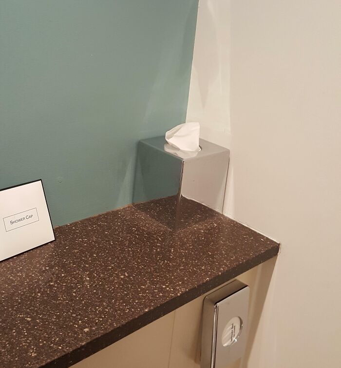 Tissue box matching surroundings with reflective surface blending into wall and countertop in a bathroom setting.