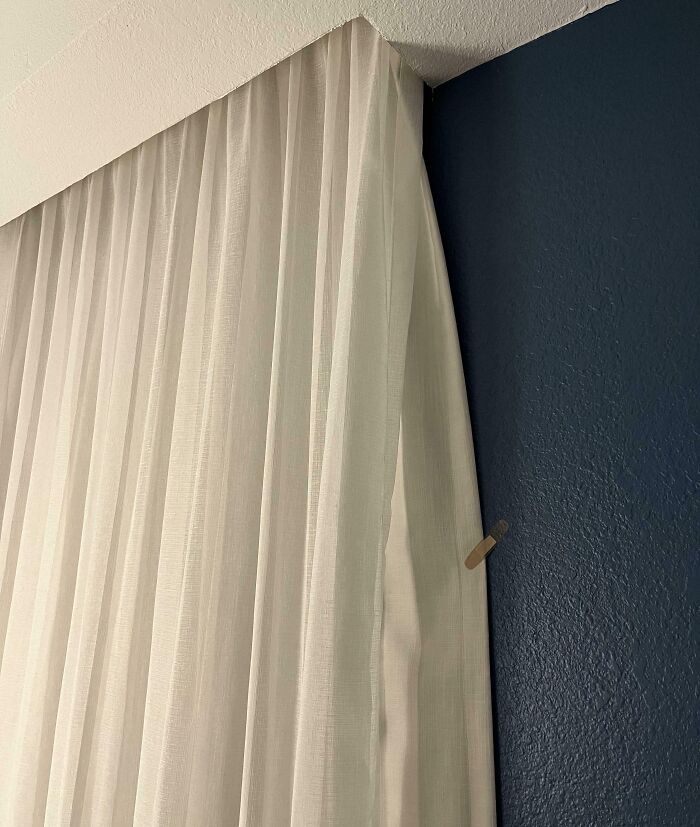 Sheer curtains neatly hung on a blue wall corner using a clothespin as a genius life hack for securing fabric.