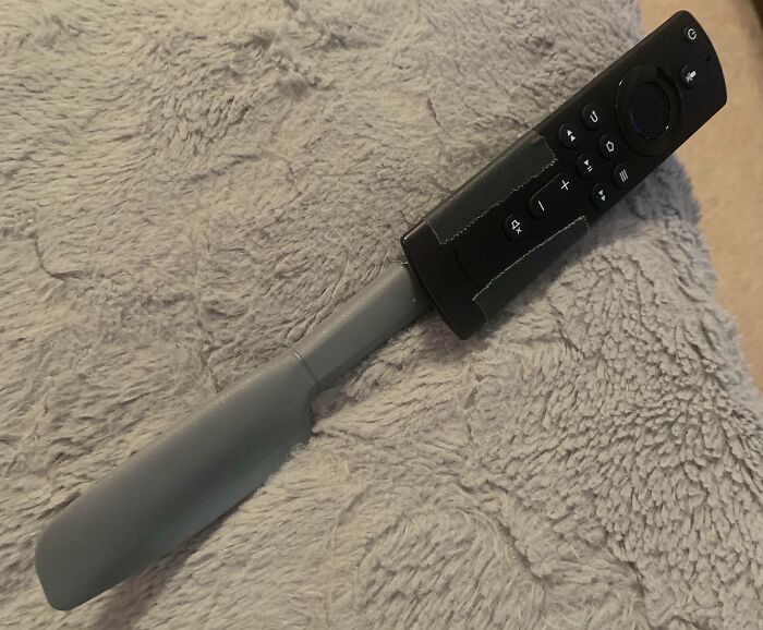 Remote control attached to a spatula handle as a clever genius life hack for easier grip and use on a soft fabric surface.