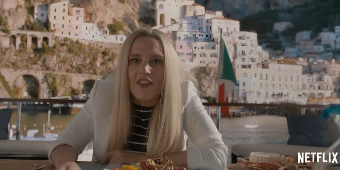 Young woman with long blonde hair dining outdoors with coastal buildings in the background, representing Netflix movies letdowns.