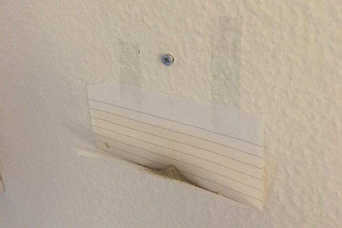 Wall with a small hole covered by a piece of lined paper showing a simple genius life hack for damage concealment.