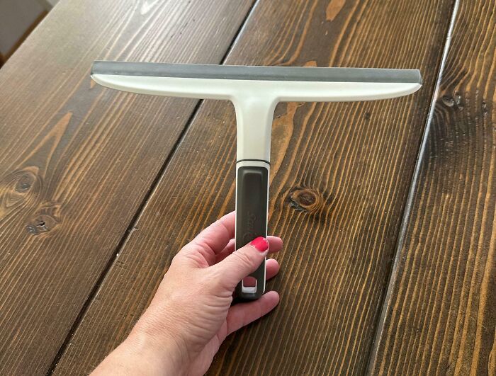 Hand holding a window squeegee on a wooden surface demonstrating a genius life hack for easy cleaning.