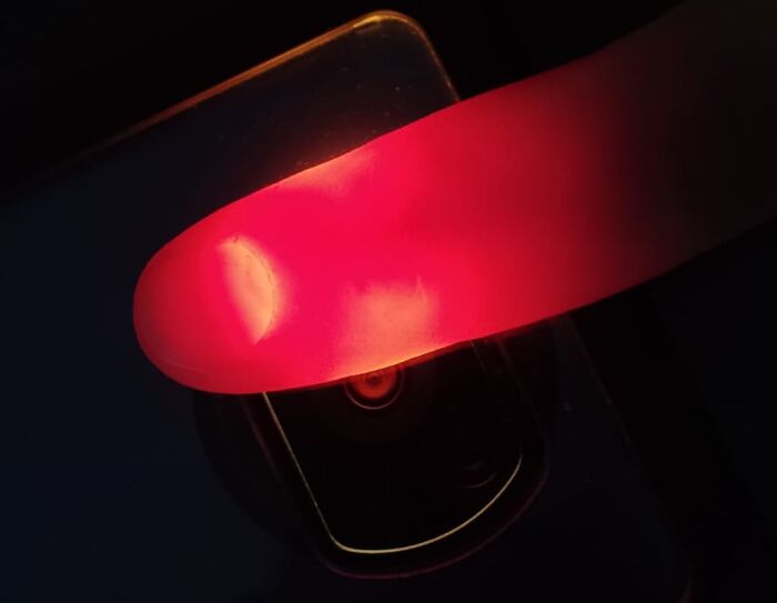Close-up of a finger held over a phone flashlight, demonstrating a genius life hack for a DIY red light effect.