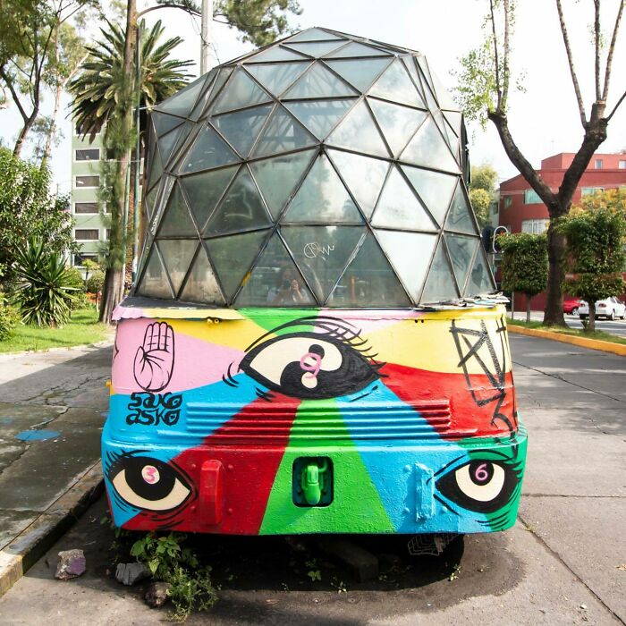 Colorful mural by Colombian artist SakoAsko featuring large eyes and geometric patterns on a street installation.