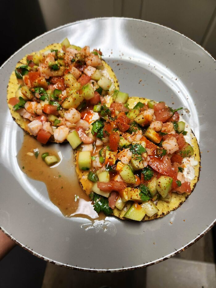 Two tostadas topped with shrimp, diced vegetables, and sauce on a gray plate showcasing restaurant worker orders.