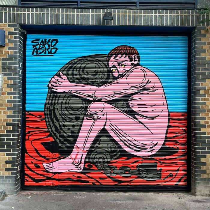 Mural by Colombian artist SakoAsko showing a pink figure hugging a black textured object with a blue and red background.