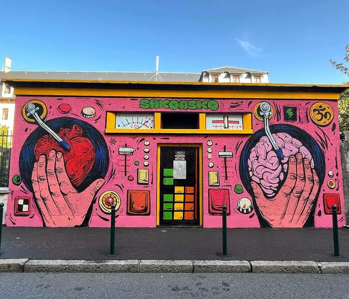 Colorful mural by Colombian artist SakoAsko depicting hands holding a heart and brain, blending fantasy and reality themes.
