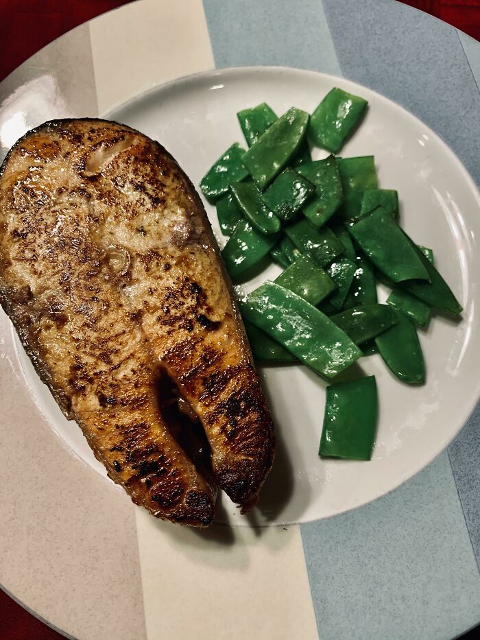 Grilled fish fillet served with cooked green snap peas on a plate, showcasing restaurant workers' patience with unusual orders.