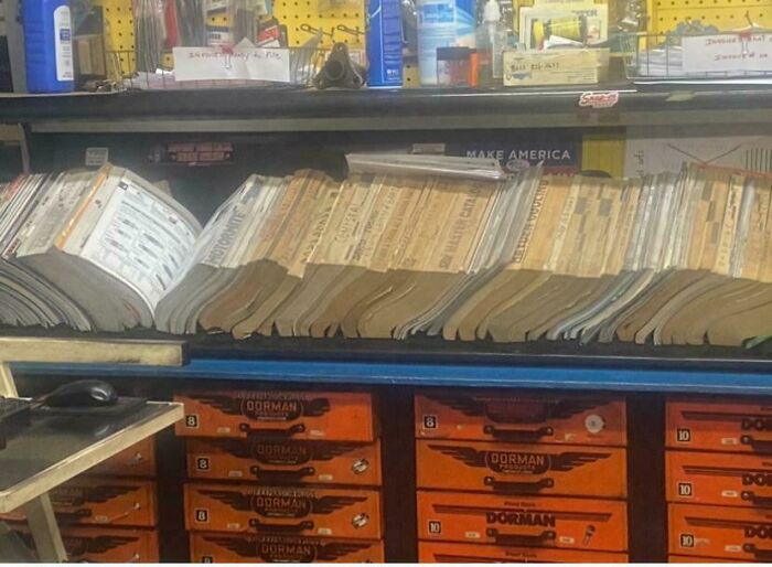 Car mechanics' worn repair manuals open on a workbench surrounded by tools and parts in a garage setting.