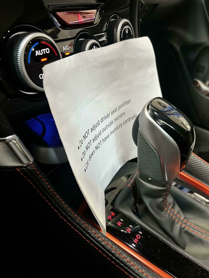 Car mechanics taking a photo of a car gear shift and dashboard with a warning note taped nearby inside the vehicle.