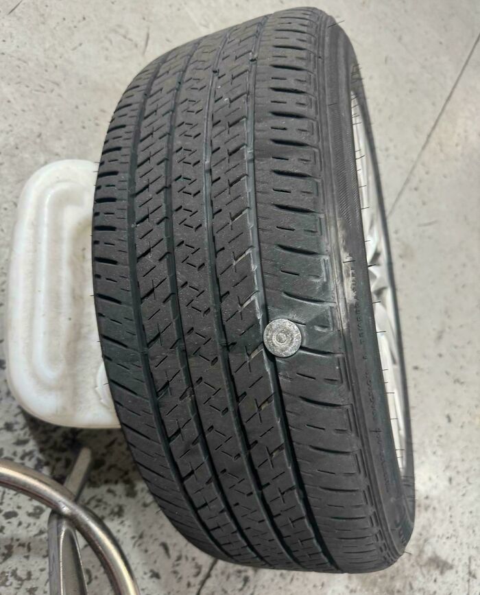 Car mechanic shows a tire with a large s***w stuck in the tread, proving unusual tire damage for others to believe.