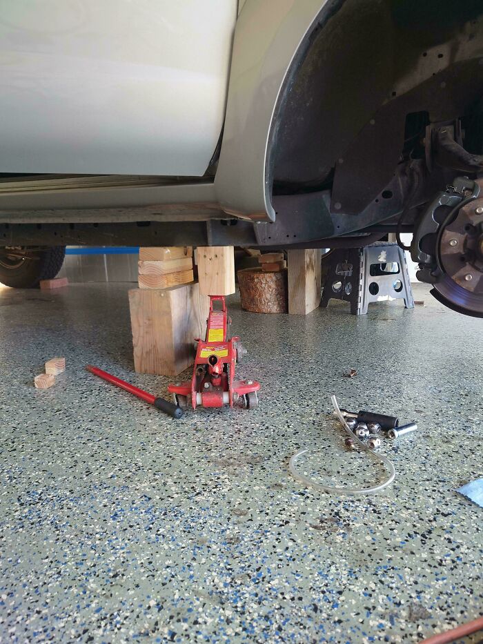 Car mechanics using wooden blocks and a jack to support a raised vehicle during repair work in a garage.