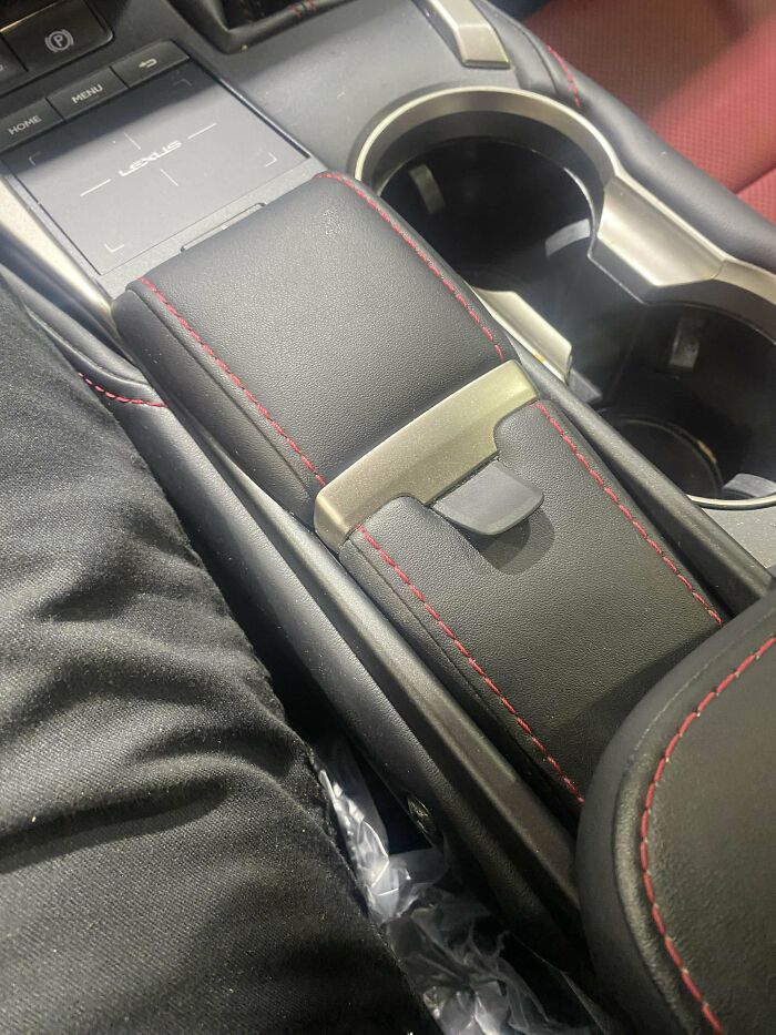 Car mechanics showing close-up of a Lexus car interior center console and armrest with red stitching details.
