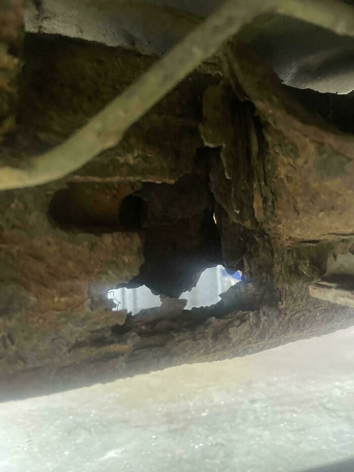 Close-up of rusted car frame with large hole, showing damage car mechanics documented to prove issues.