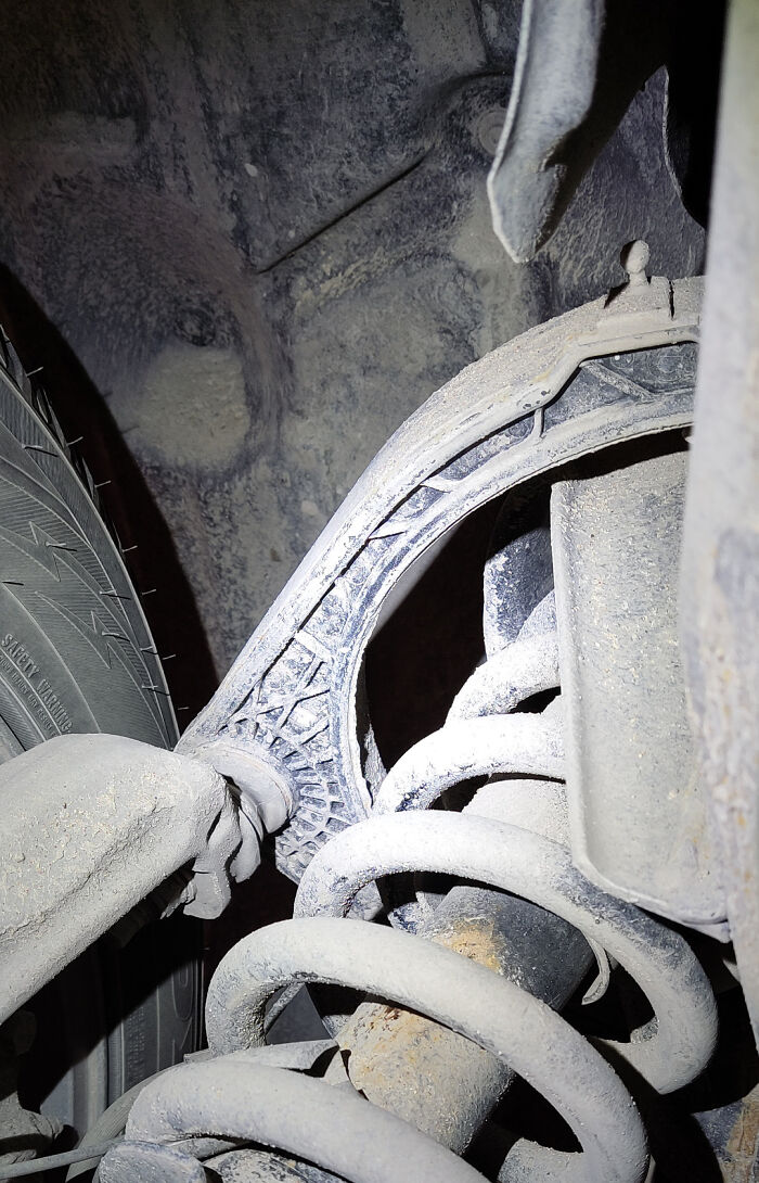 Close-up of a broken car suspension coil and damaged control arm taken by a mechanic for evidence.