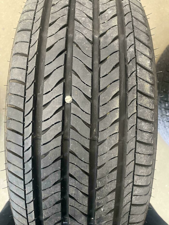 Close-up of a car tire with a nail embedded, showing a mechanic's photo to prove the issue clearly.
