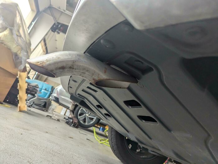Exhaust pipe extending unusually far from the rear of a car, captured by a car mechanic in a workshop.