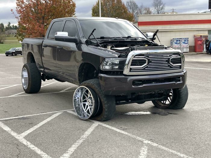 Pickup truck with front wheel completely detached, showcasing a challenging car mechanic situation in a parking lot.