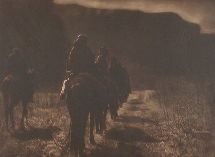 Silhouettes of riders on horses traveling through a dimly lit landscape, capturing a moment of 20th century history.