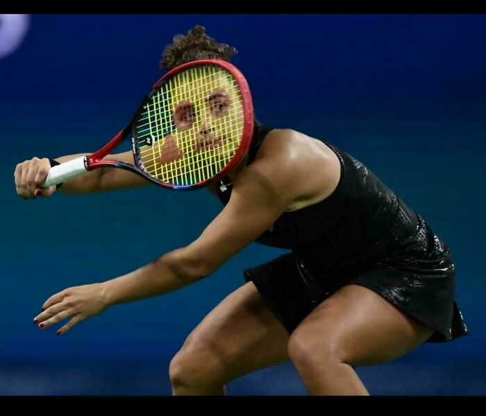Tennis player with racket perfectly framing face, creating an accidental renaissance photo moment during a match.